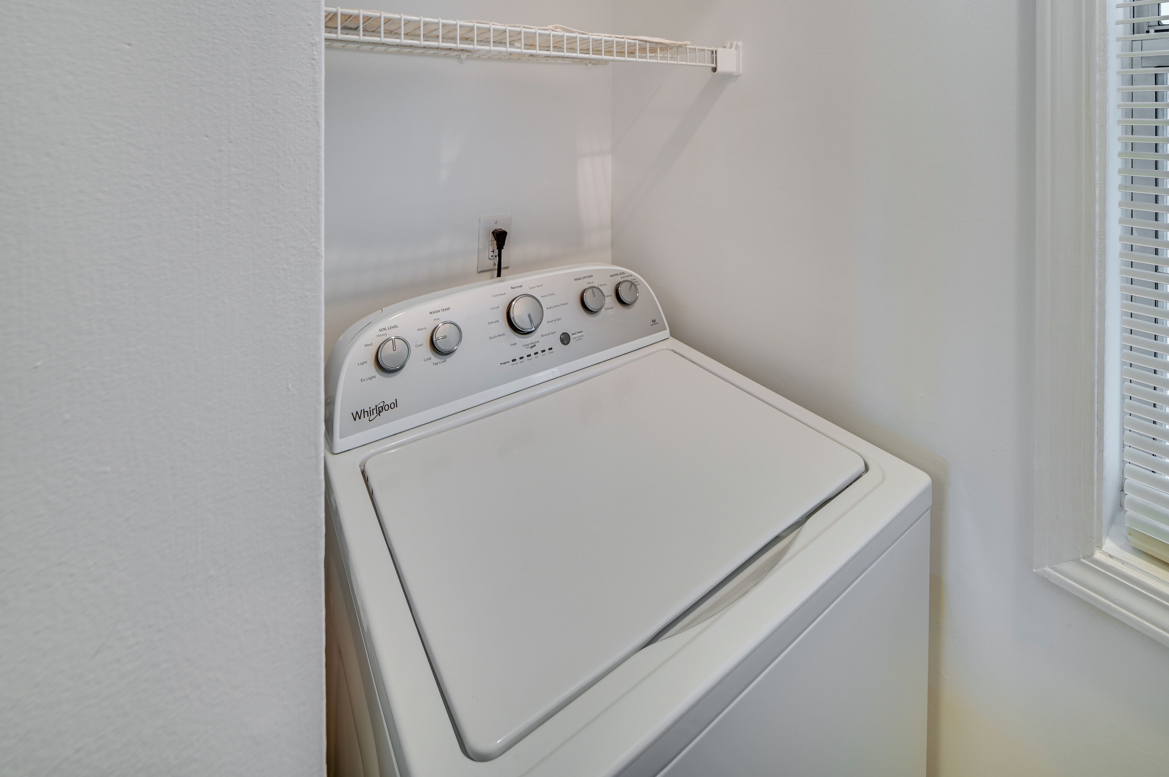 A front-loading Whirlpool washer in a white-walled laundry room with a window on the right.