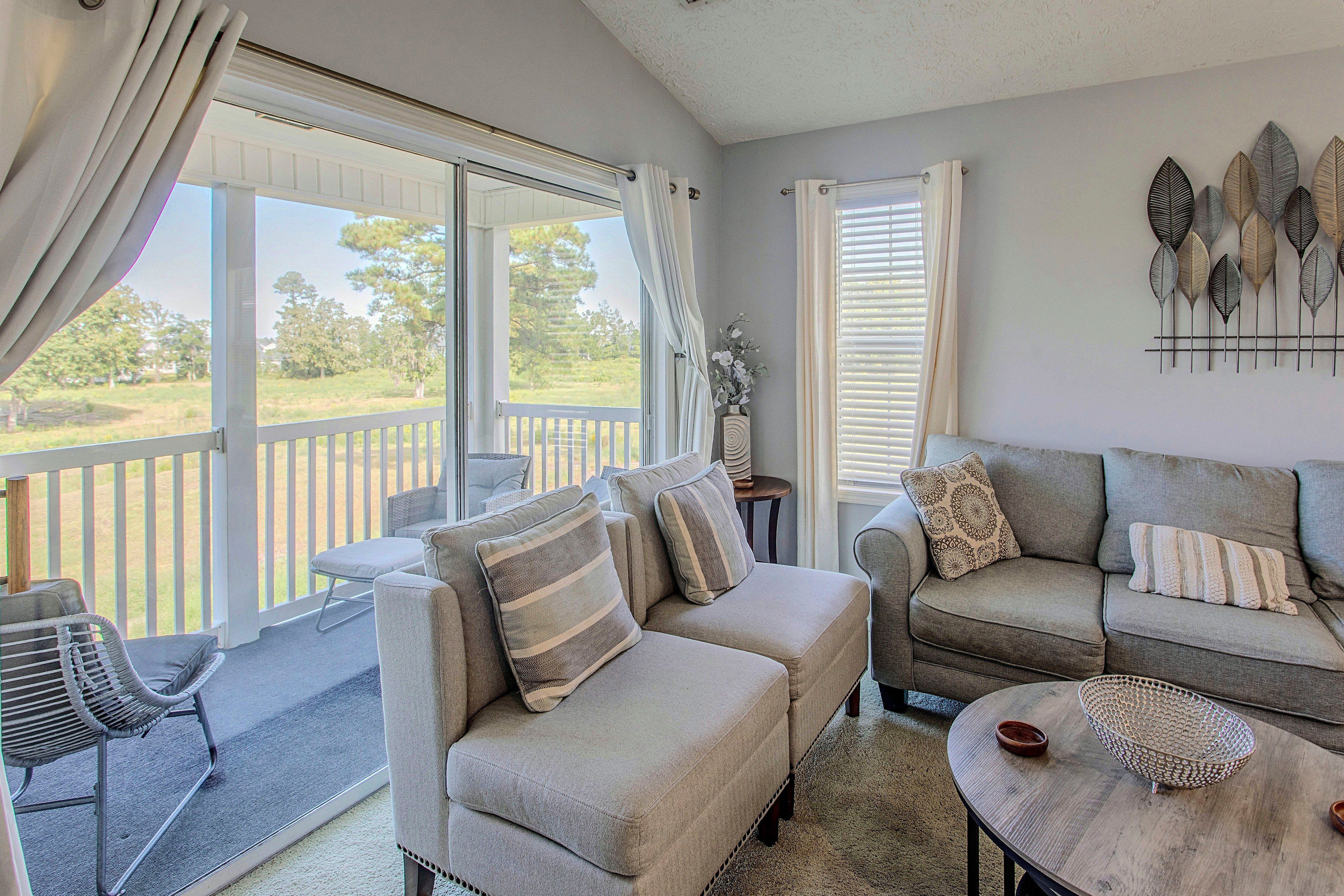 A living room with a sofa, armchairs, a coffee table, and a view of a deck and trees.