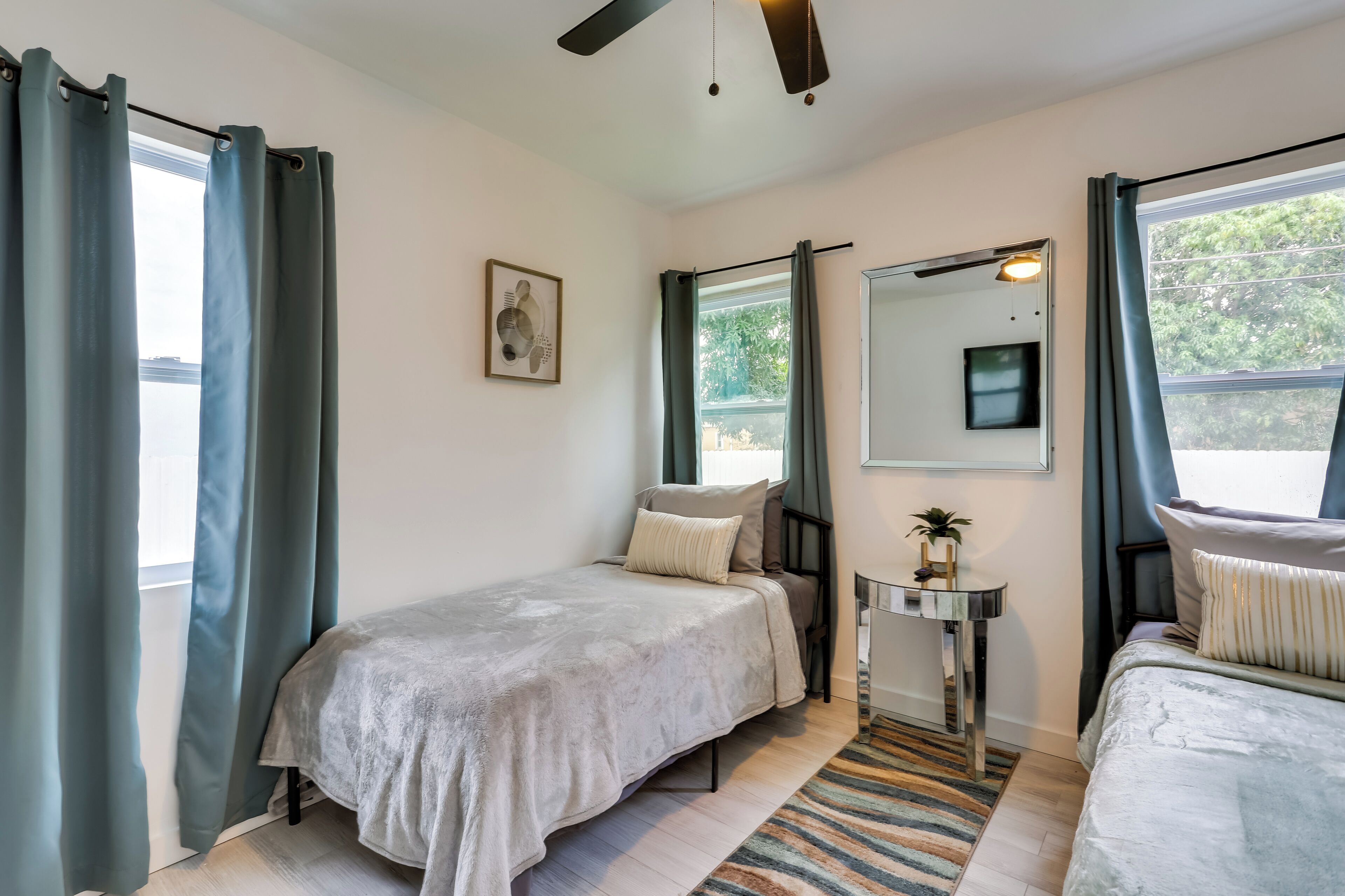 Un dormitorio con dos camas, una mesita, un espejo y una ventana con cortinas.