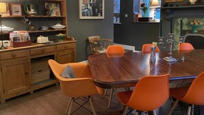 Un coin repas avec une table en bois et des chaises orange, un buffet en bois orné d’assiettes décoratives et un tableau accroché au mur.