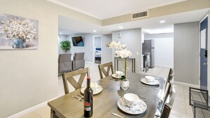 Comedor con una mesa de madera dispuesta para cuatro personas, una botella de vino y un florero con flores blancas.