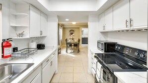 Una cocina moderna con armarios blancos, una estufa negra y un comedor al fondo.