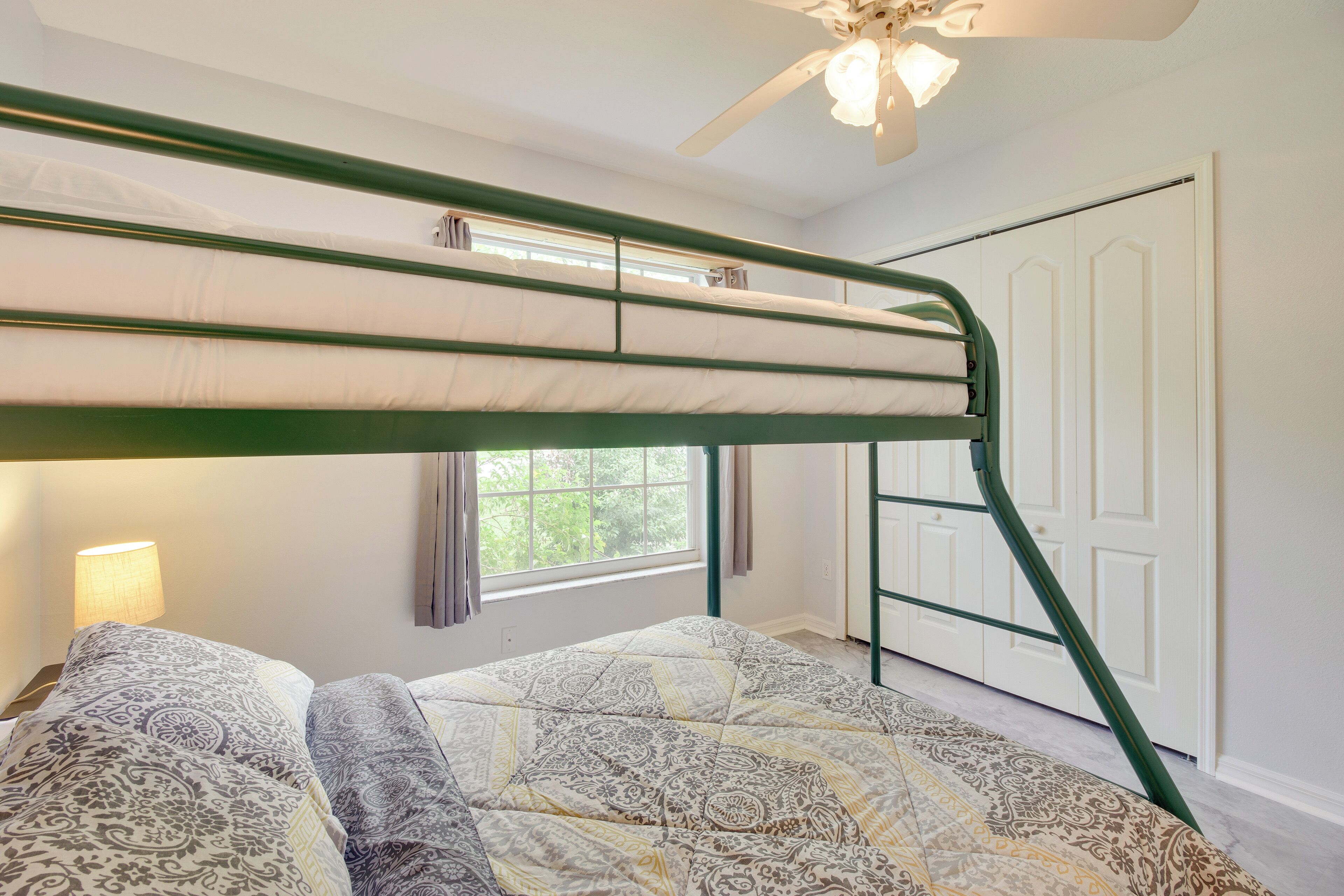 A bunk bed with a green frame, a patterned bedspread, and a ceiling fan.