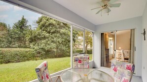 A covered patio with a glass table and floral chairs, a ceiling fan, and a view of a garden and house. - 20 Mi to Disney: Condo w/ Pool Access in Clermont! (Clermont)