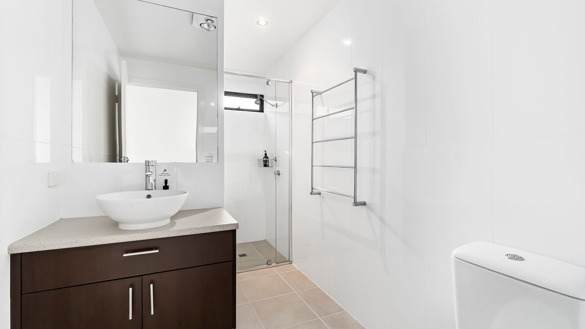 Et moderne badeværelse med en hvid vask, mørke træskabe, en brusekabine i glas og et hvidt toilet.