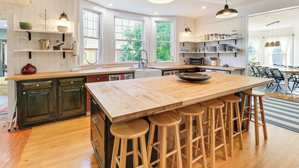 A modern kitchen with a large island, wooden stools, and pendant lighting. - Historic Bar Harbor Home ~ 2 Blocks to Main St! (Bar Harbor)