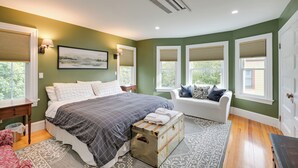 A bedroom with a large bed, a chest of drawers, a white sofa, and a window with blinds. - Historic Bar Harbor Home ~ 2 Blocks to Main St! (Bar Harbor)
