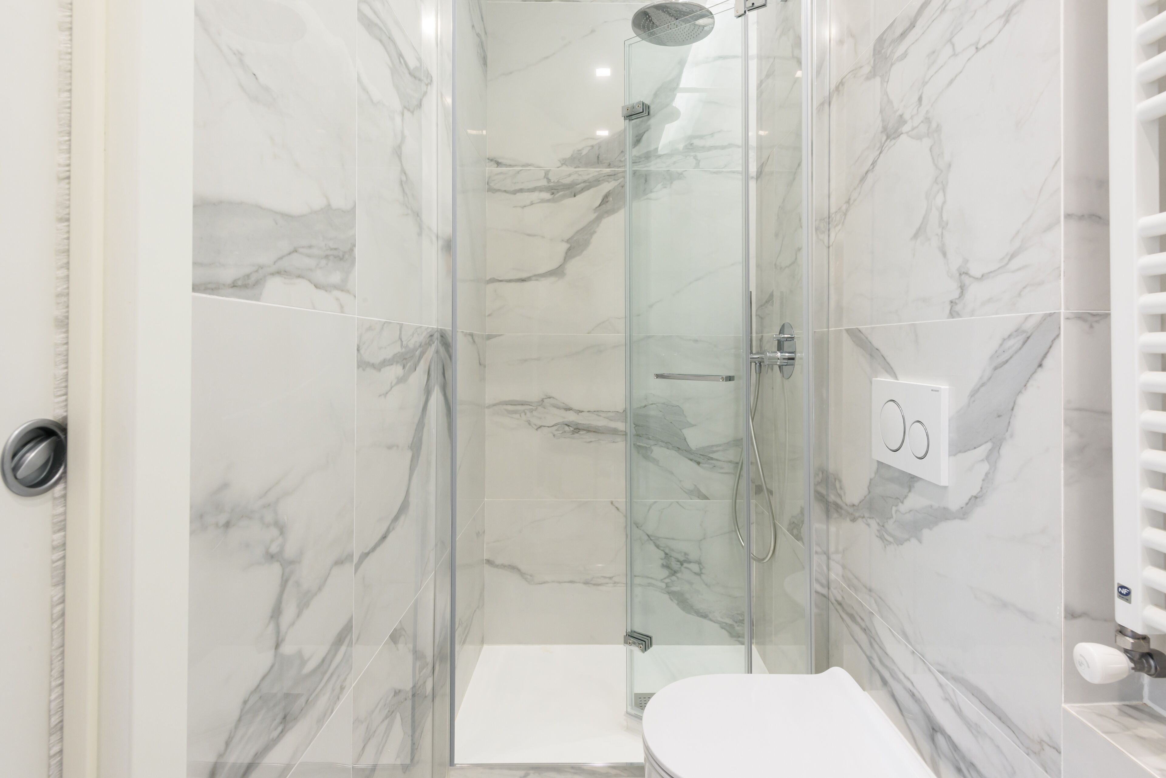 A modern bathroom with marble walls, a glass shower enclosure, and a white toilet.
