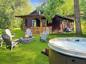 Eine Holzhütte mit Veranda, Sitzgelegenheiten im Freien, einem Feuerkorb und einem Whirlpool.