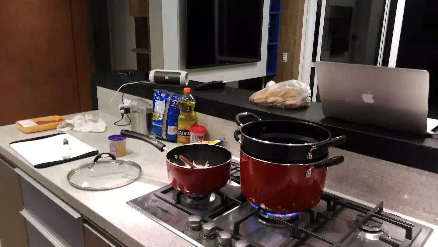 A kitchen with two red pots on the stove, a laptop, and various kitchen items on the counter.