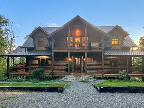 A two-story log cabin with a porch, a covered front entrance, and a gravel driveway. - Tipsy Bear Lake House - Luxury Log home in premiere gated community + free railroad and rafting (Bryson City)