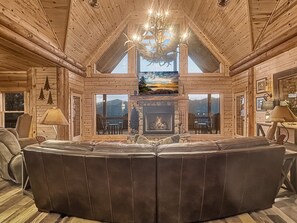 A log cabin interior with a fireplace, leather seating, and a chandelier. - Tipsy Bear Lake House - Luxury Log home in premiere gated community + free railroad and rafting (Bryson City)