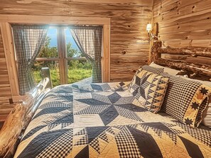 A wooden cabin bedroom with a large bed, plaid curtains, and a view of greenery outside. - Tipsy Bear Lake House - Luxury Log home in premiere gated community + free railroad and rafting (Bryson City)
