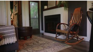 A cozy living room with a fireplace, a rocking chair, a patterned rug, and a small table. - White Oak Creek Cabin (Harrison)