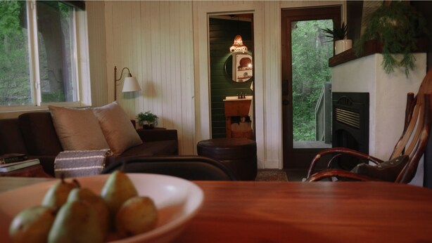 A cozy living room with a wooden table, a sofa, a lamp, and a fireplace. - White Oak Creek Cabin (Harrison)