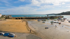 A coastal beach scene with boats, a stone pier, and a sandy shore. - Harbour Side (St Ives)