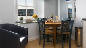 A dining area with a table set for two, a potted plant, a vase with flowers, and a bottle of wine. - Harbour Side (St Ives)