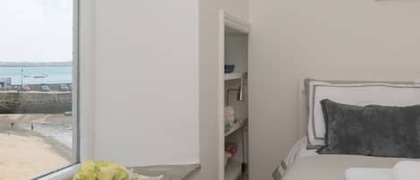 A bedroom with a bed, a window with a view of the sea, and a shelf with items.