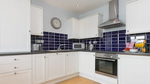 A modern kitchen with white cabinets, a stainless steel range hood, a microwave, and a sink. - Harbour Side (St Ives)