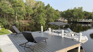 A wooden dock with a boat, lounge chairs, and a canopy.