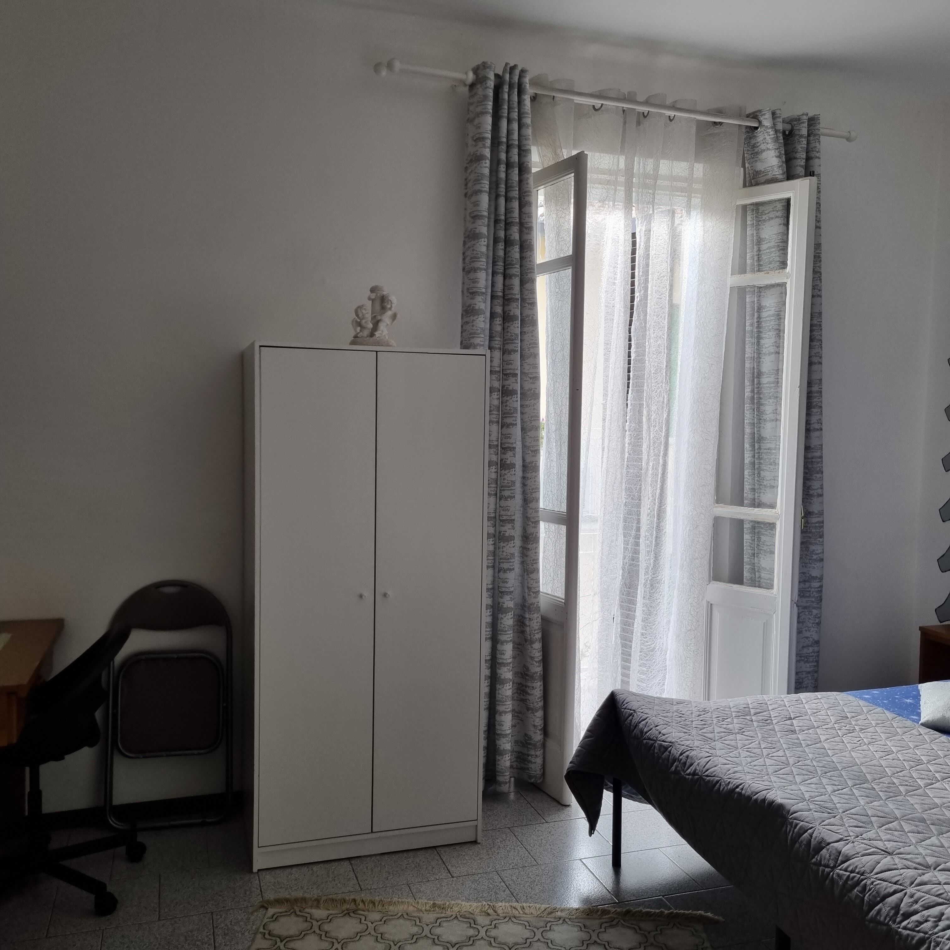 Un dormitorio con cama, armario, escritorio y ventana con cortinas.
