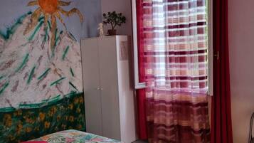 Ein Schlafzimmer mit Bett, Kleiderschrank, Fenster mit Vorhängen und Wandbild.