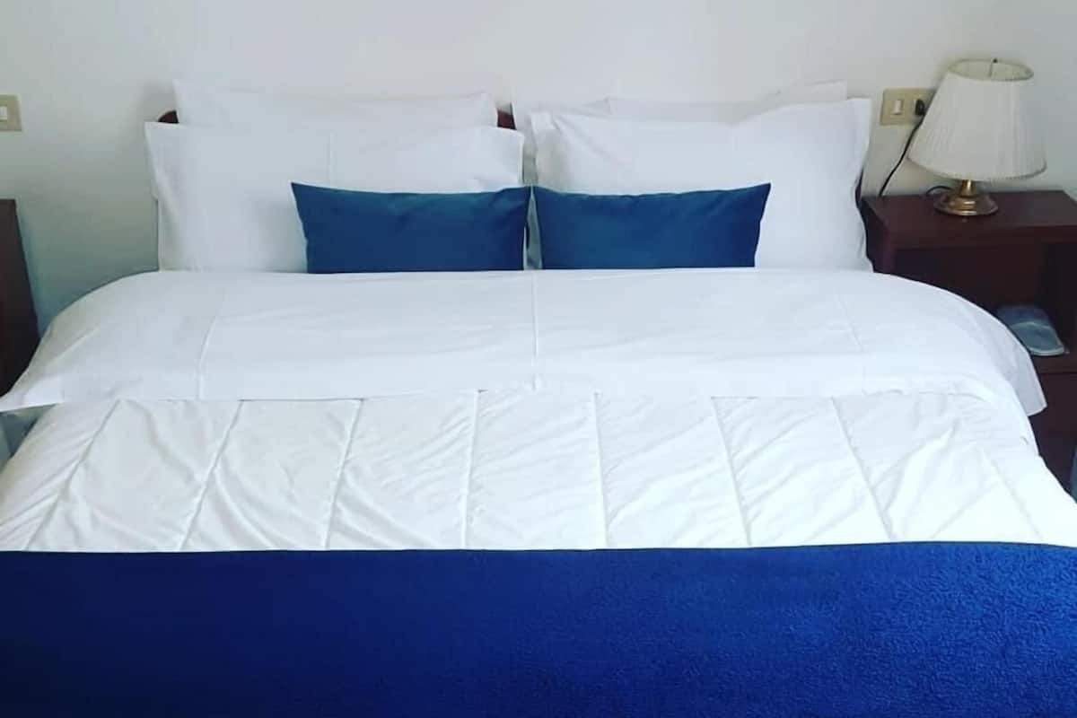 Un lit avec une literie blanche et bleue, une tête de lit en bois et une table de chevet avec une lampe.