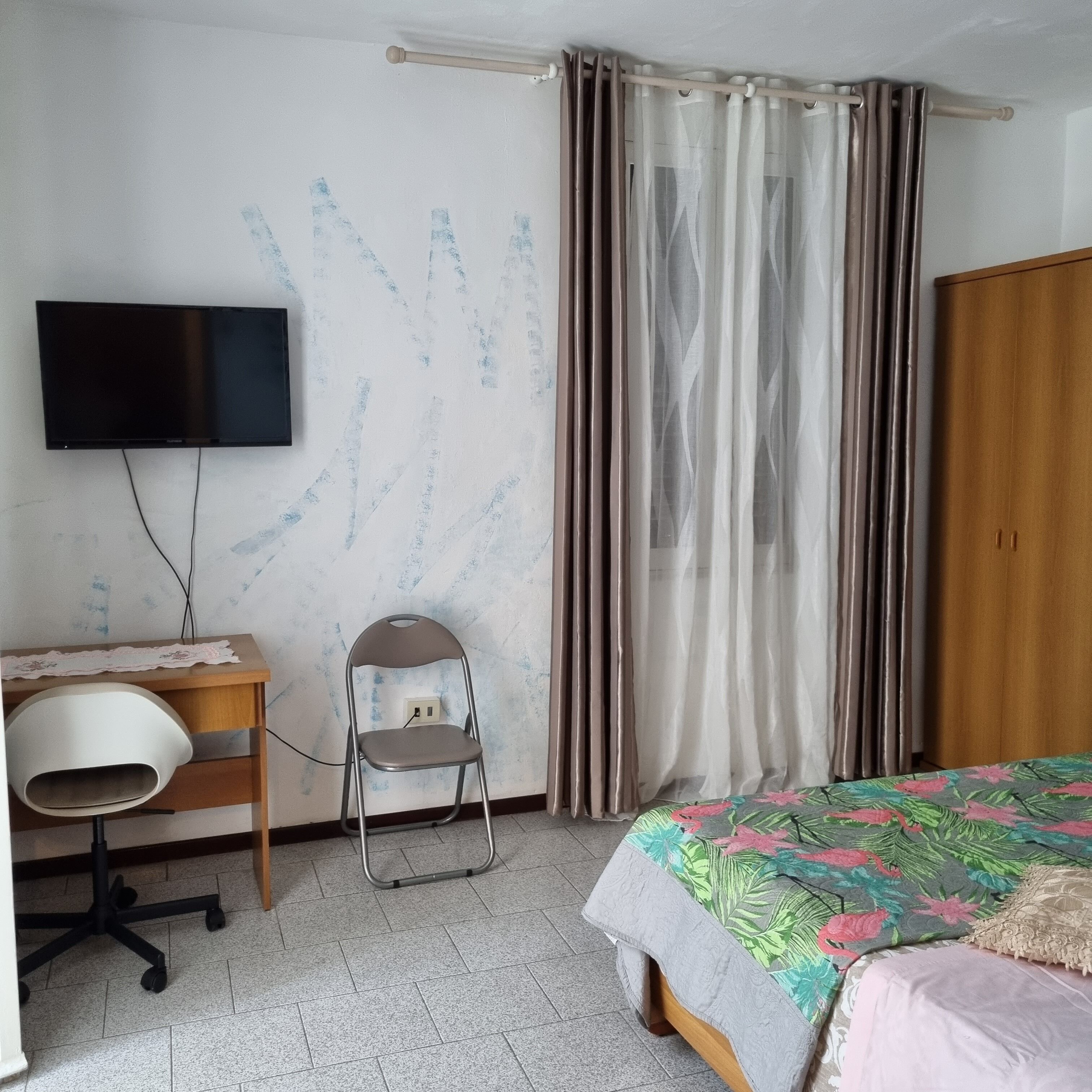 A bedroom with a bed, a desk with a chair, a television, and a wardrobe.