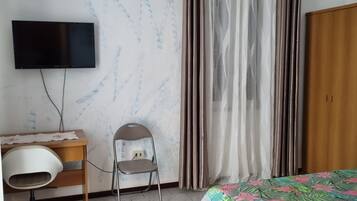 A bedroom with a bed, a desk with a chair, a television, and a wardrobe.