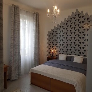 Een slaapkamer met een bed, gordijnen, een kroonluchter en een behang met een patroon.