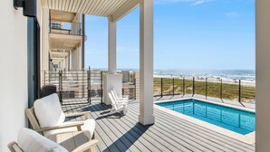 A wooden deck with a pool, white chairs, and a view of the ocean.