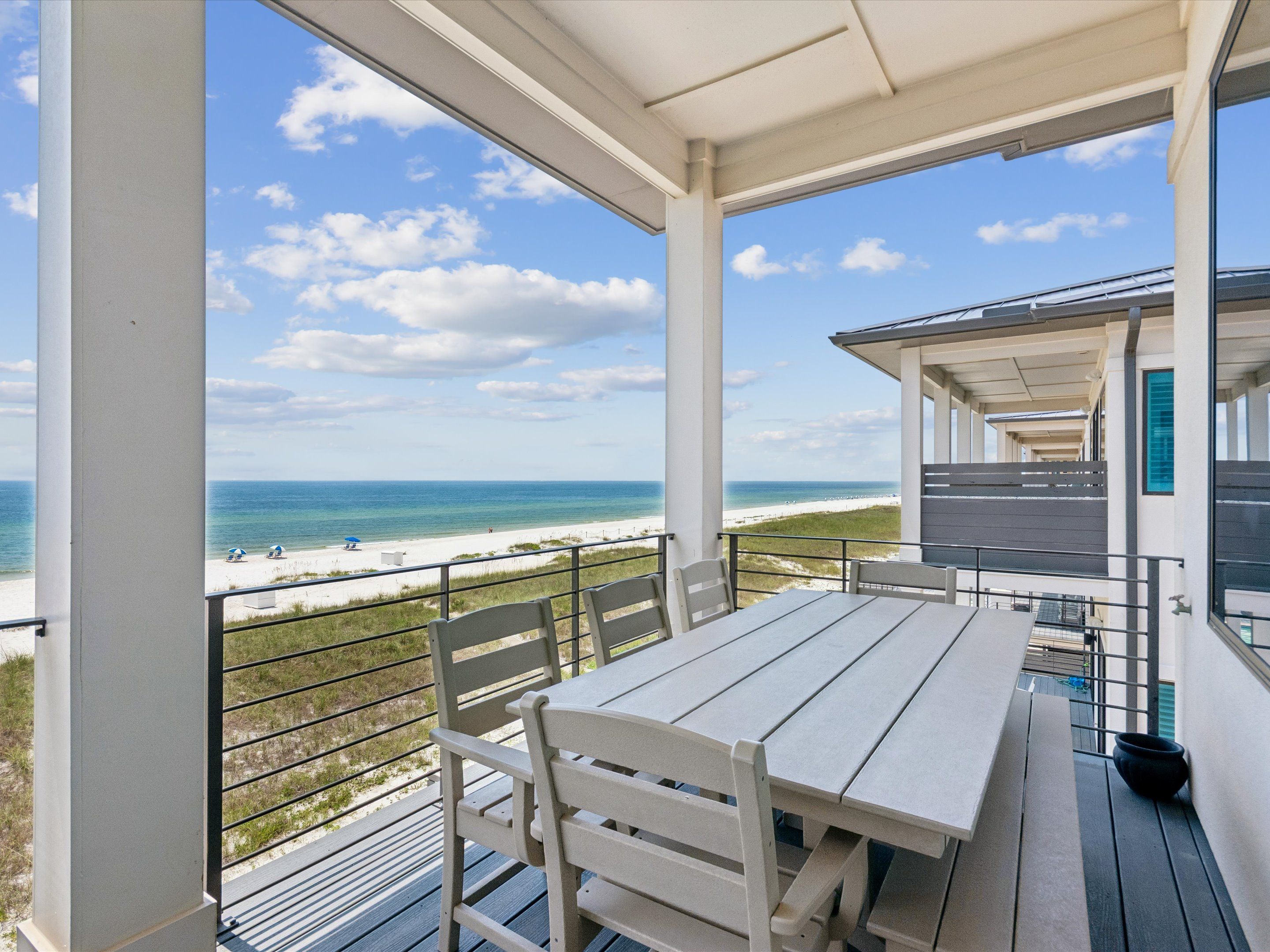 A covered outdoor area with a table and chairs, overlooking a beach with a clear sky.