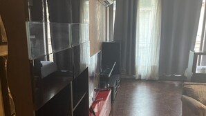 A living room with a wooden floor, a red entertainment unit, a flat-screen TV, and a large window with curtains.
