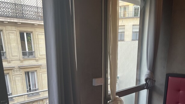 A hotel room with a large window, a bed with white bedding, and a red headboard.