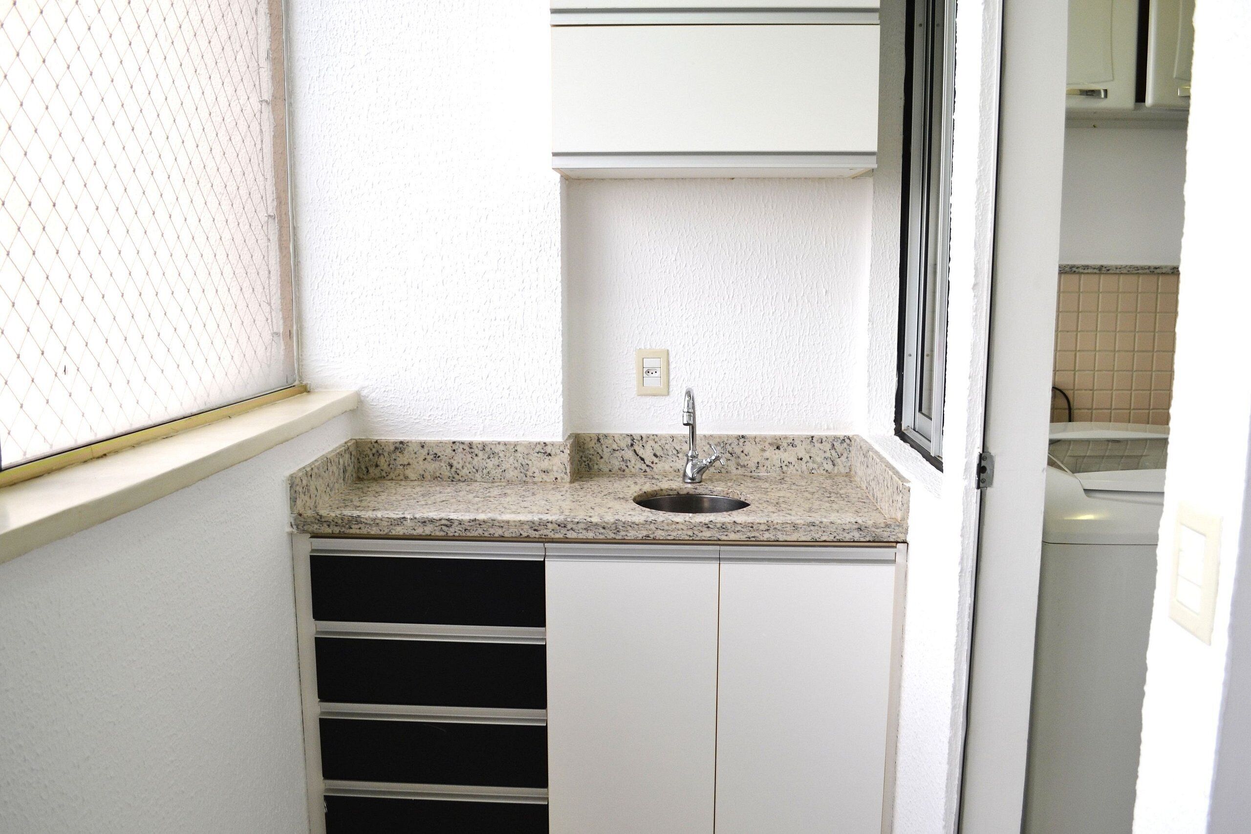 A small kitchen with a granite countertop, a stainless steel sink, and white cabinets.