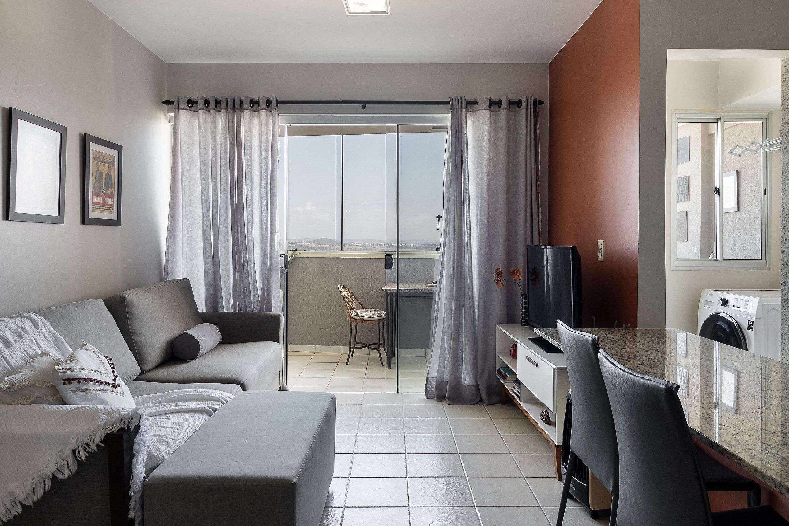 Una sala de estar moderna con sofá, una mesa de comedor, sillas, televisor y un balcón con cortinas.