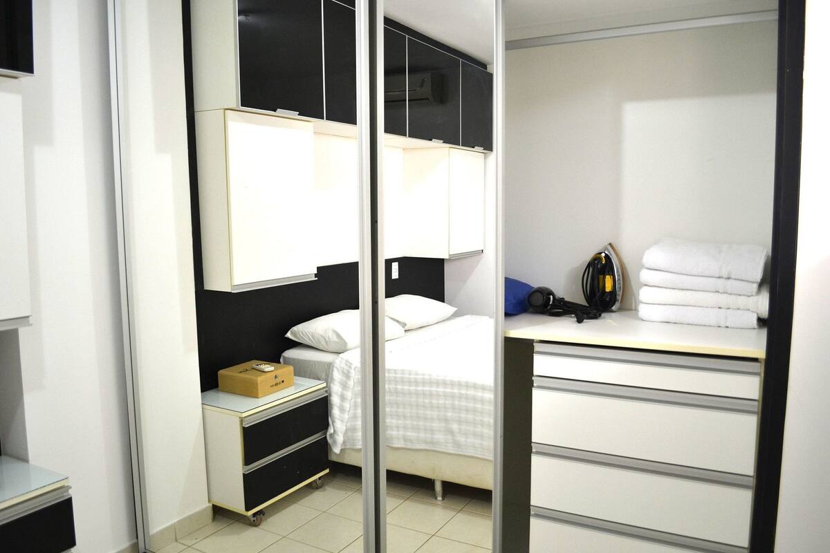 Una habitación de hotel con cama, escritorio, armario y un mueble pequeño.