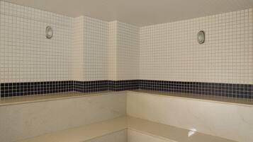 Casa de banho com paredes revestidas de azulejos brancos, faixa decorativa em mosaico preto e branco e bancada bege.