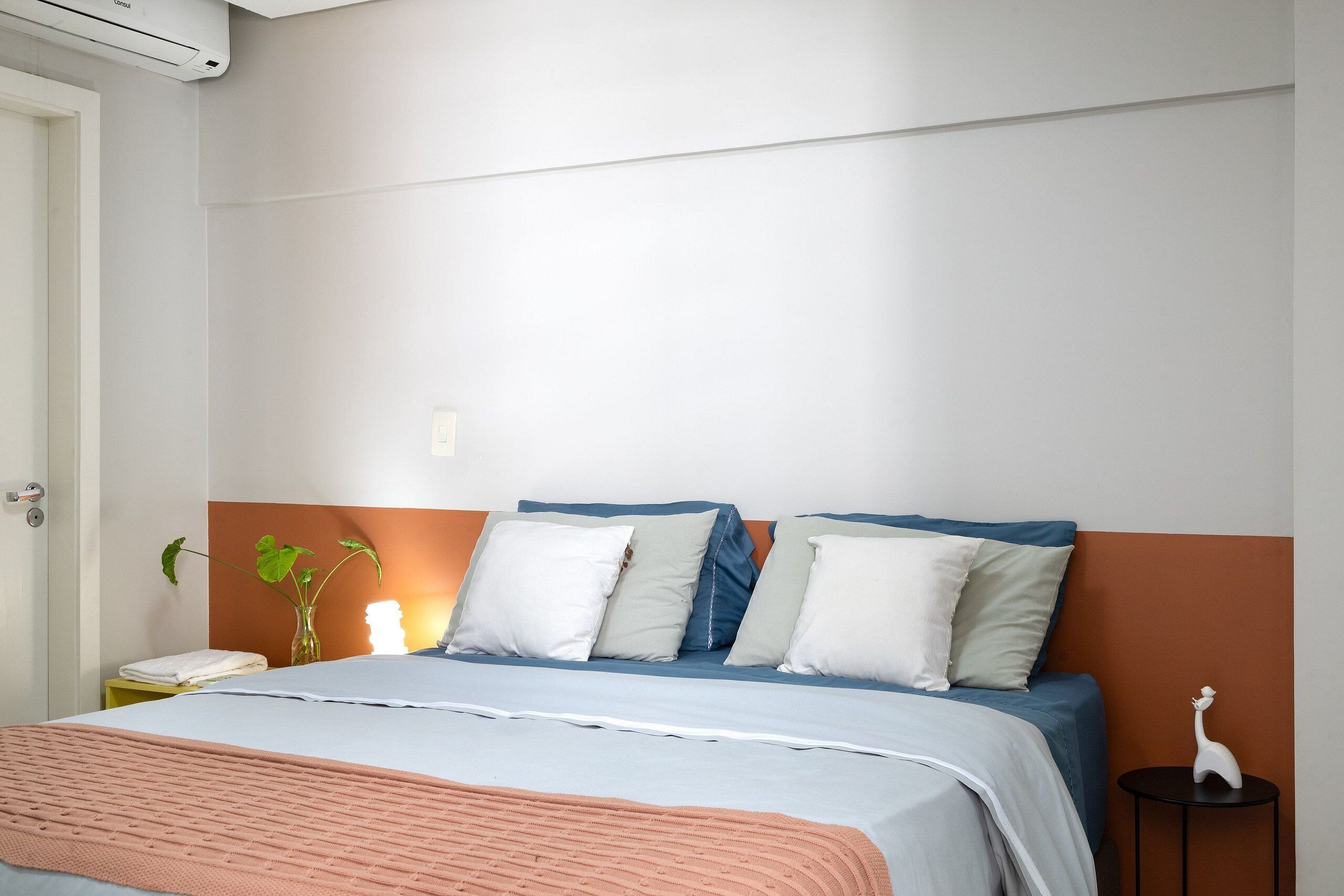 A bedroom with a bed, pillows, a bedside table, a vase with a plant, and a small statue.