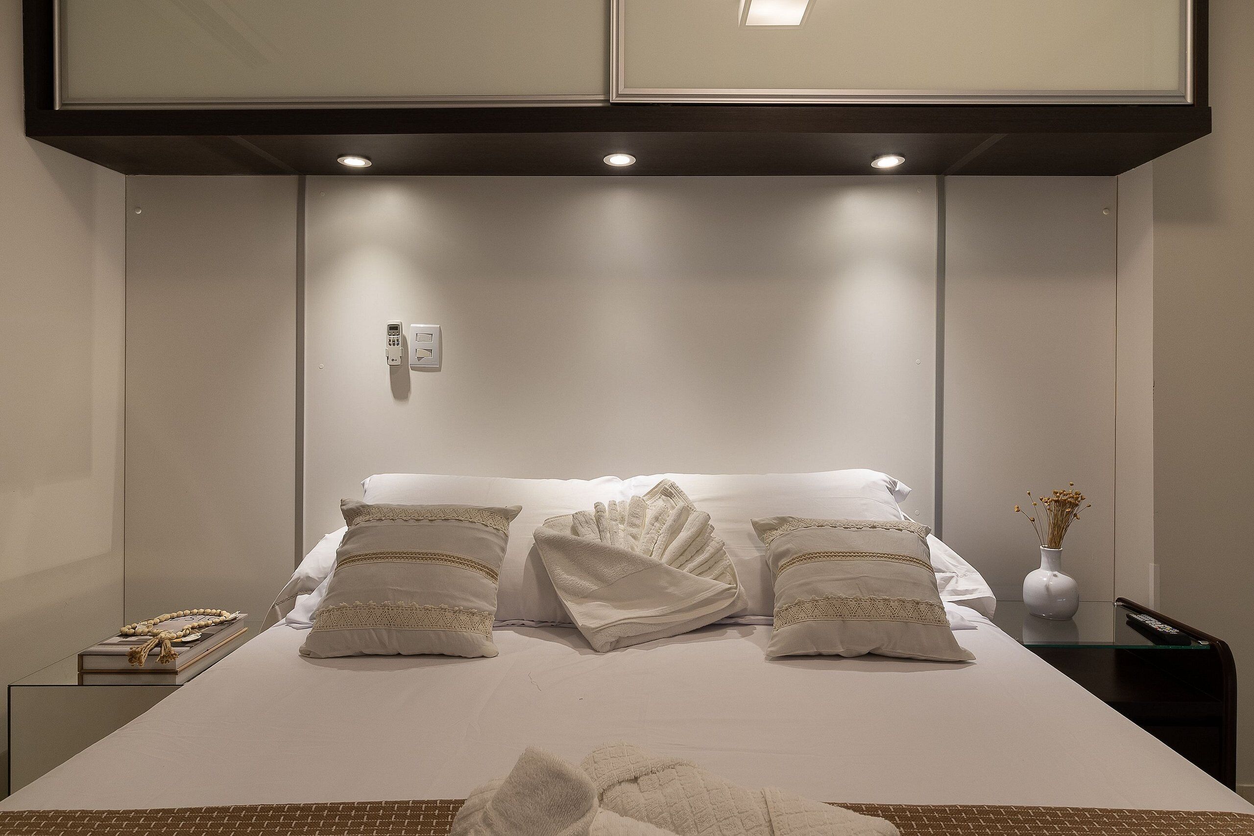 A hotel room with a neatly made bed, a bedside table with a remote control, and a wall-mounted phone.