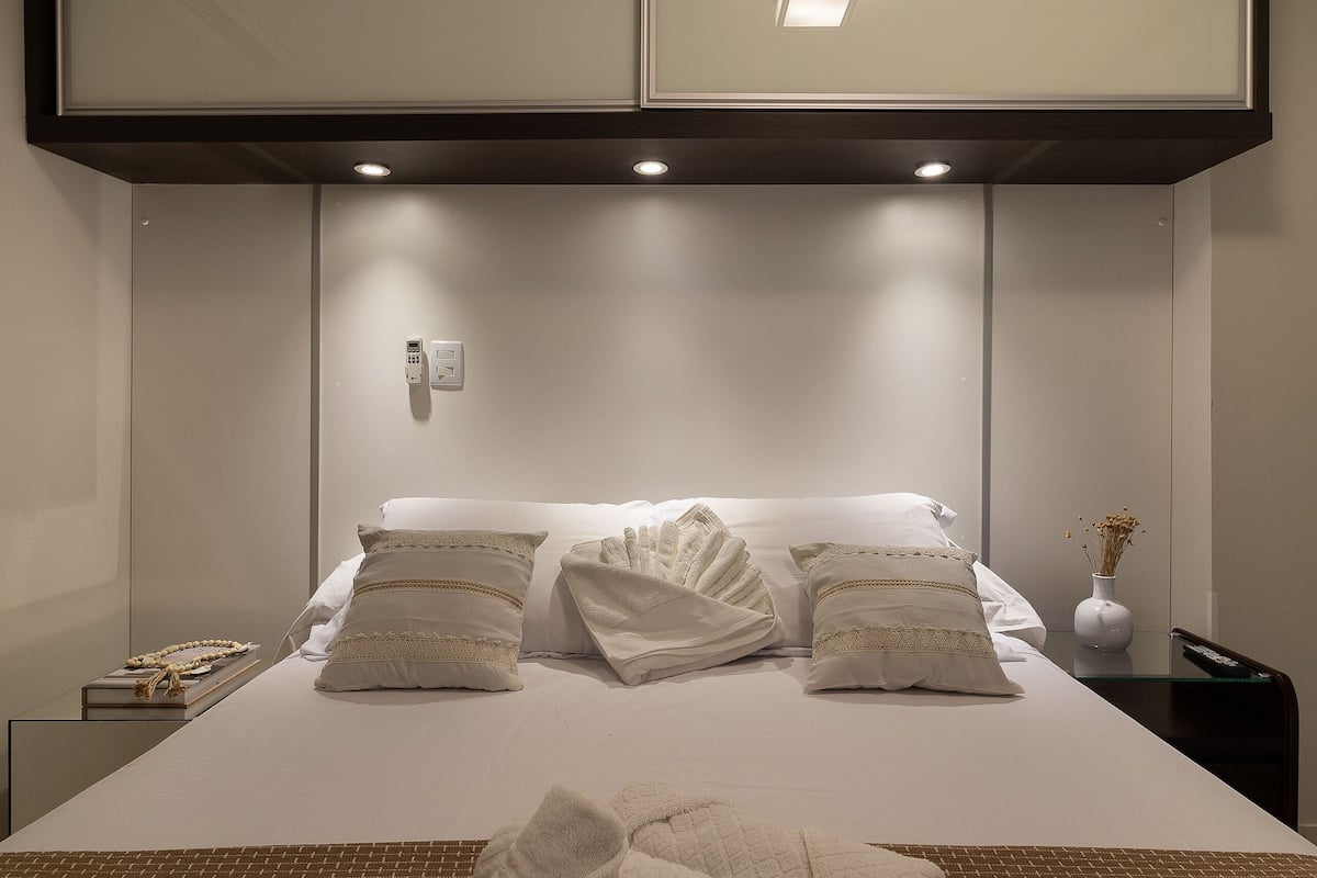 Habitación de hotel con una cama bien tendida, una mesita de noche con control remoto y un teléfono en la pared.