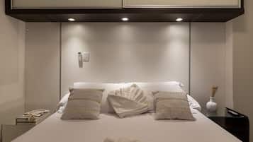 A hotel room with a neatly made bed, a bedside table with a remote control, and a wall-mounted phone.