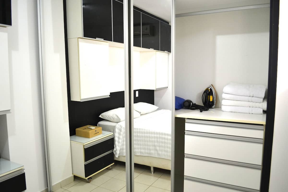 Una habitación de hotel con cama, escritorio, armario y un mueble pequeño.