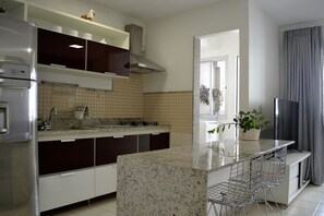 A modern kitchen with a central island, stainless steel appliances, and a dining area with bar stools. - UNIQUE RESIDENCE (Goiania)