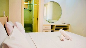 Una habitación de hotel con una cama, un espejo redondo, un tocador pequeño y una zona de ducha.