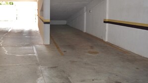 Un estacionamiento vacío con pisos y paredes de concreto, un marco de puerta visible y una línea amarilla que delimita los espacios.