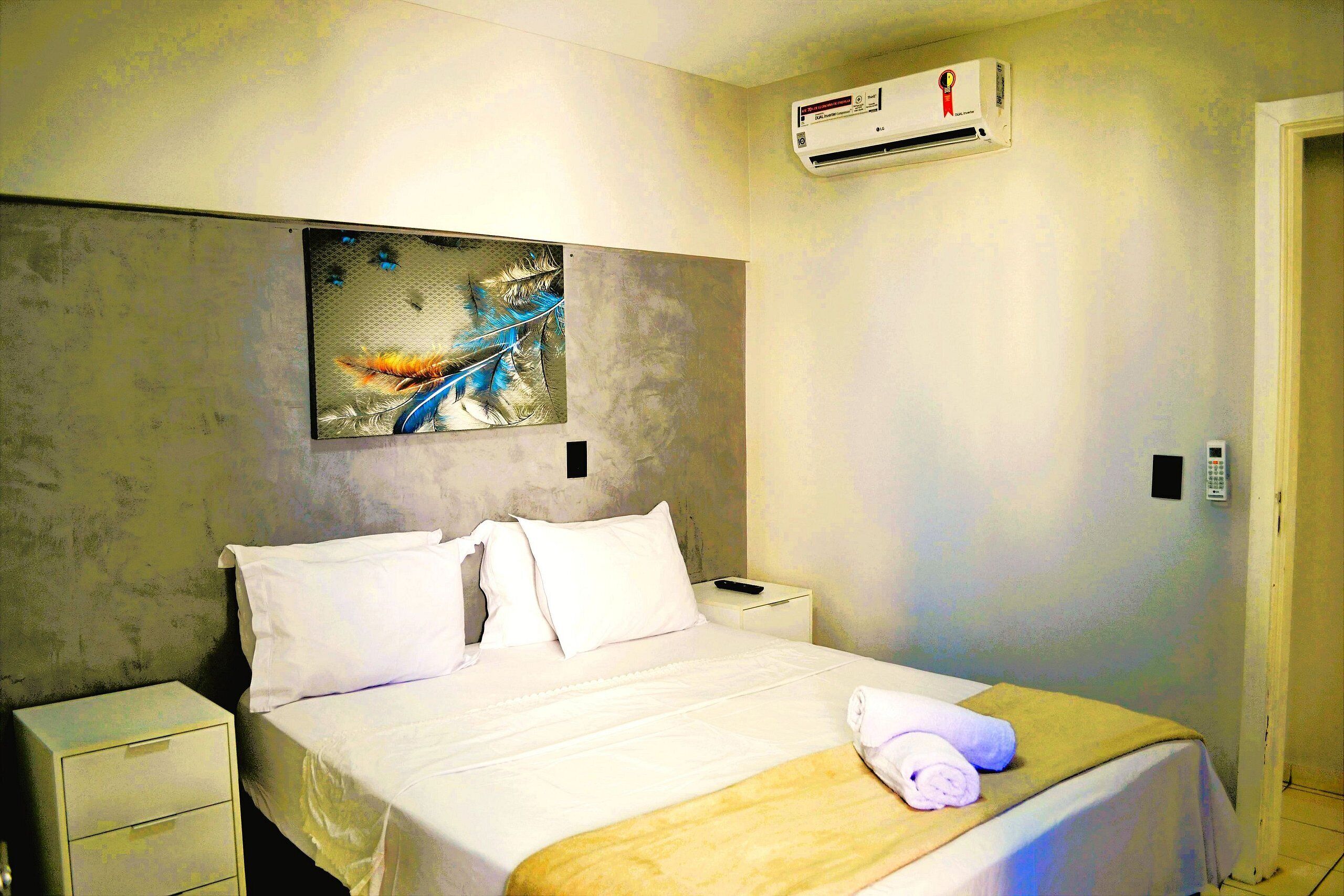 Habitación de hotel con cama, mesita de noche, aire acondicionado de pared y un cuadro sobre la cama.
