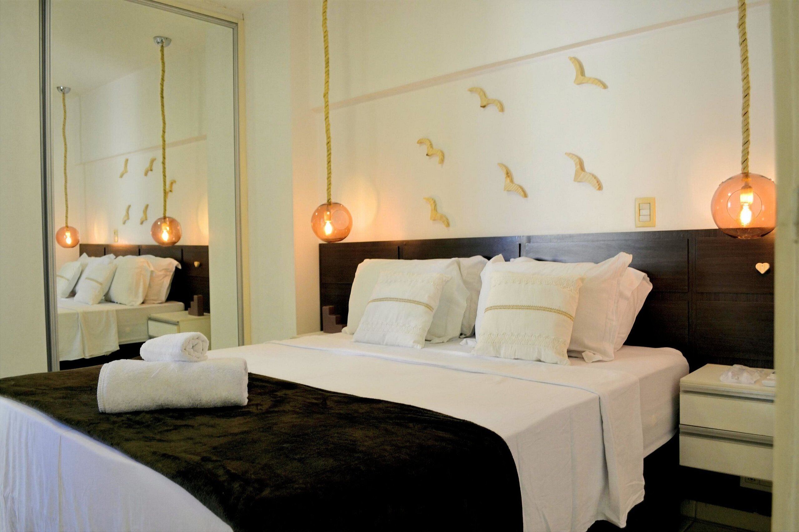 A hotel room with a bed, a nightstand, a mirror, and wall decor.