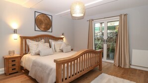 A bedroom with a wooden bed, bedside tables, a large window with curtains, and a hanging light fixture.