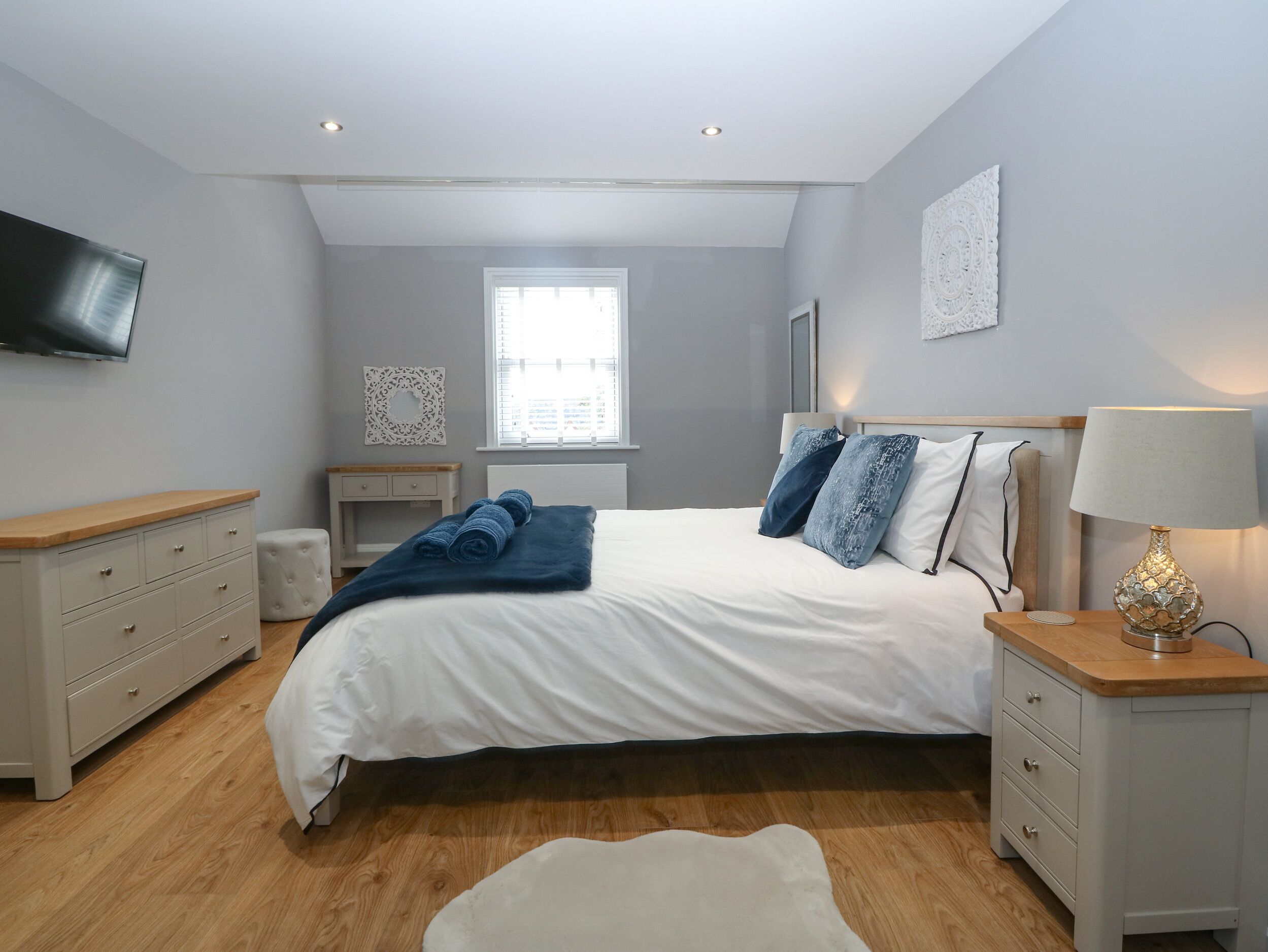 Een slaapkamer met een bed, nachtkastjes, een televisie, een raam en een lamp.